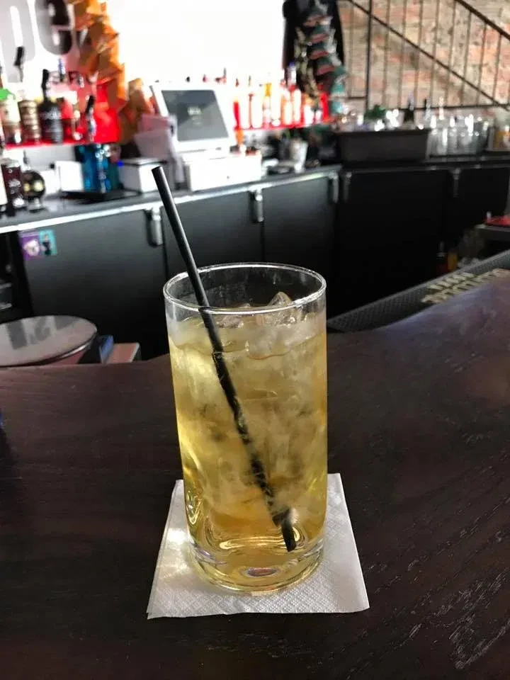 Amber drink with ice and straw on a wooden bar counter.