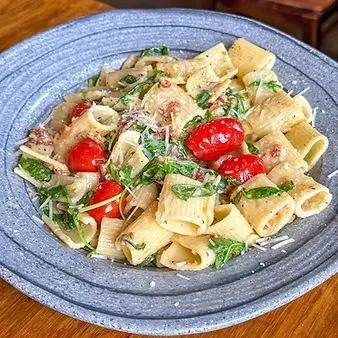 Tubular pasta with creamy sauce, cherry tomatoes, greens, and grated cheese.