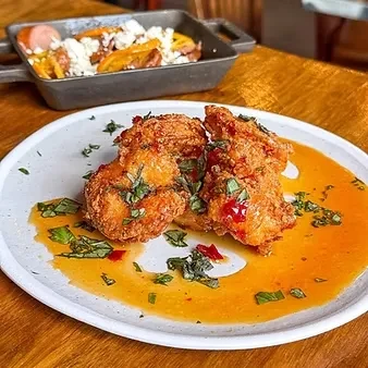 Crispy fried chicken with sauce and herbs, pan of plantains and sausage.
