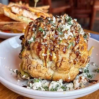 Whole roasted cauliflower topped with cheese, herbs, and dark glaze.