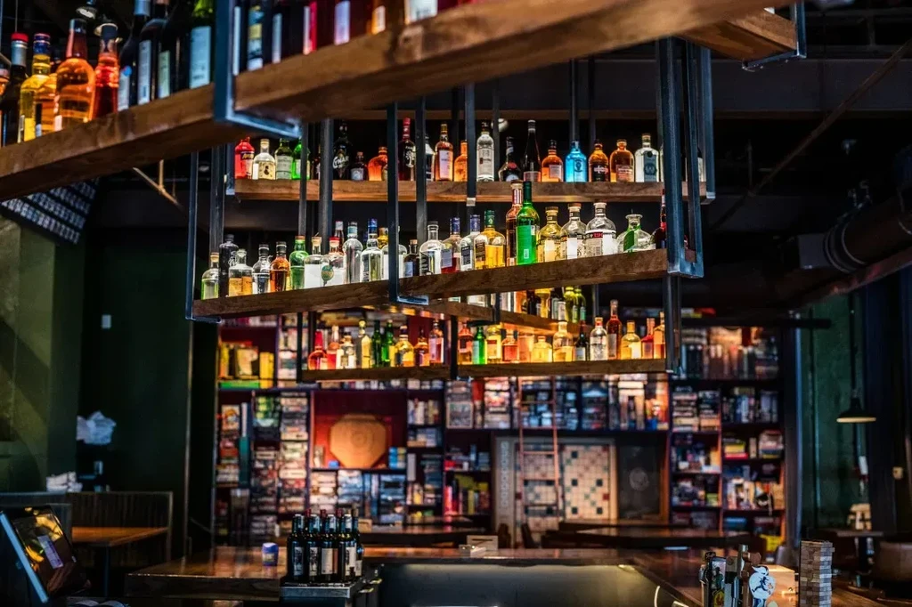 Suspended bar shelves display colorful liquor bottles, with books and games behind.