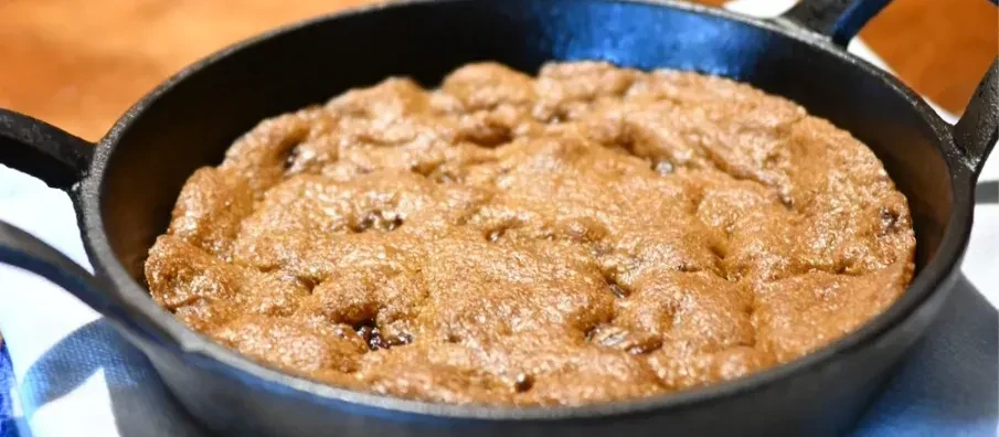 Warm golden-brown dessert with specks in a black cast iron skillet.