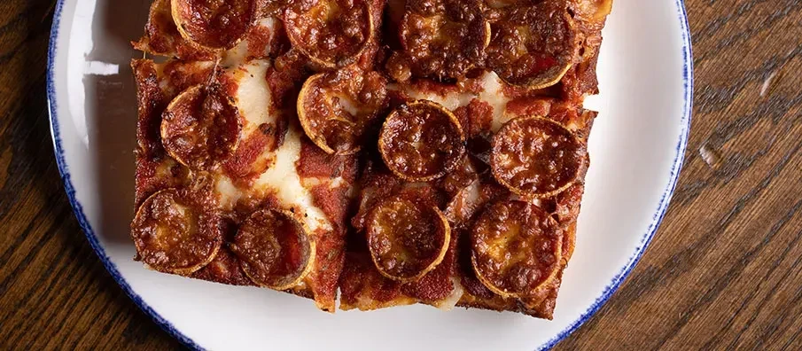 Rectangular deep-dish pizza with melted cheese and cupped pepperoni slices.