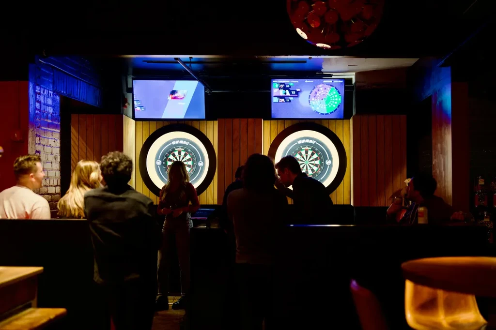 Two illuminated dartboards in a dark bar with patrons.
