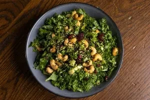Overhead view of fresh kale salad with cashews, dried berries, and seeds.