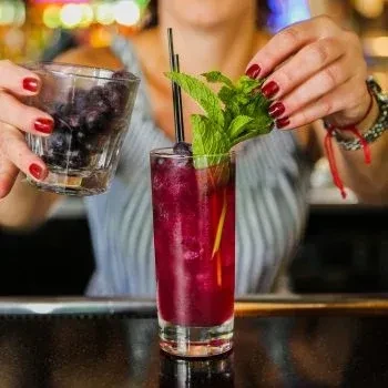 Bartender's hands garnish purple cocktail with mint and blueberries.