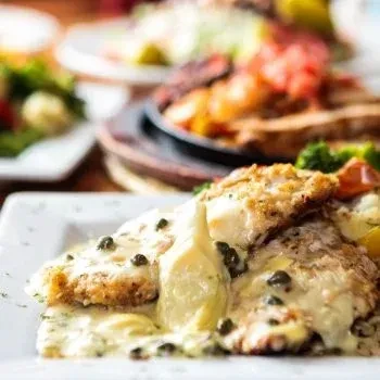 Close-up of protein with creamy caper sauce, blurred dining background.
