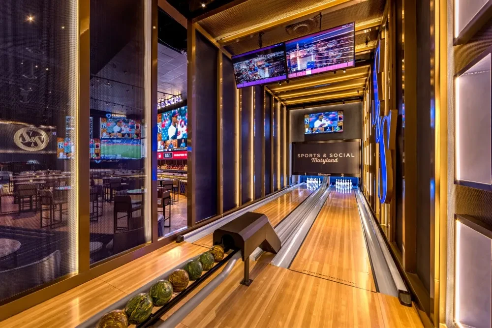 Modern bowling lane and sports bar with numerous bright sports screens.