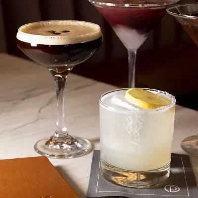 Four diverse cocktails: coffee, citrus, layered purple, and amber drinks.