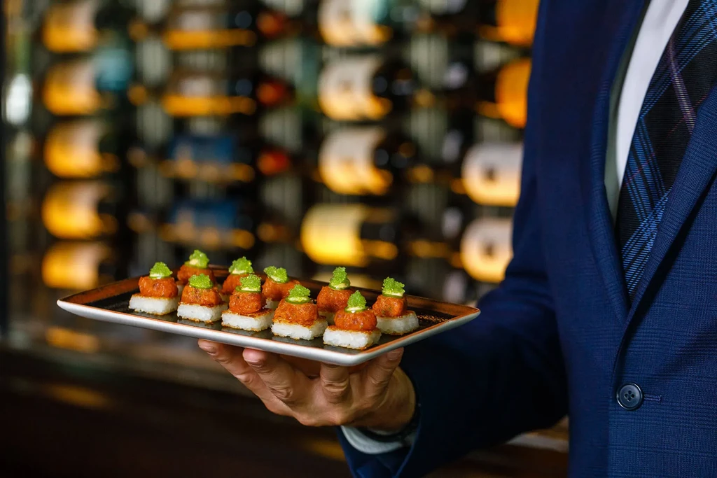 Server in suit holds tray of nine tuna and rice appetizers.