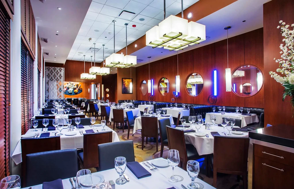 Modern, upscale dining room with dark wood paneling and set tables.