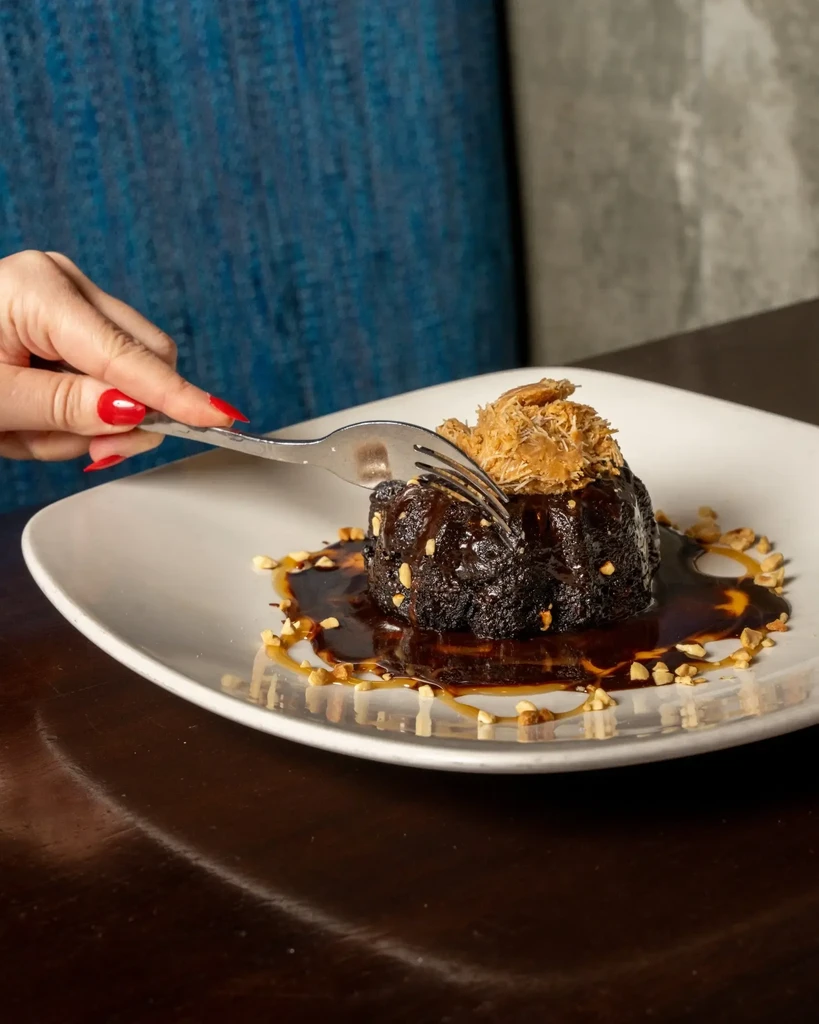 Red-nailed hand holds fork, poised over chocolate dessert with nuts.