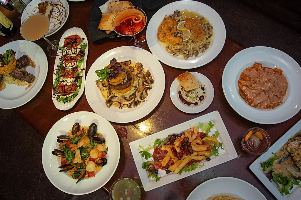 Overhead shot of a dark table laden with Italian dishes and drinks.