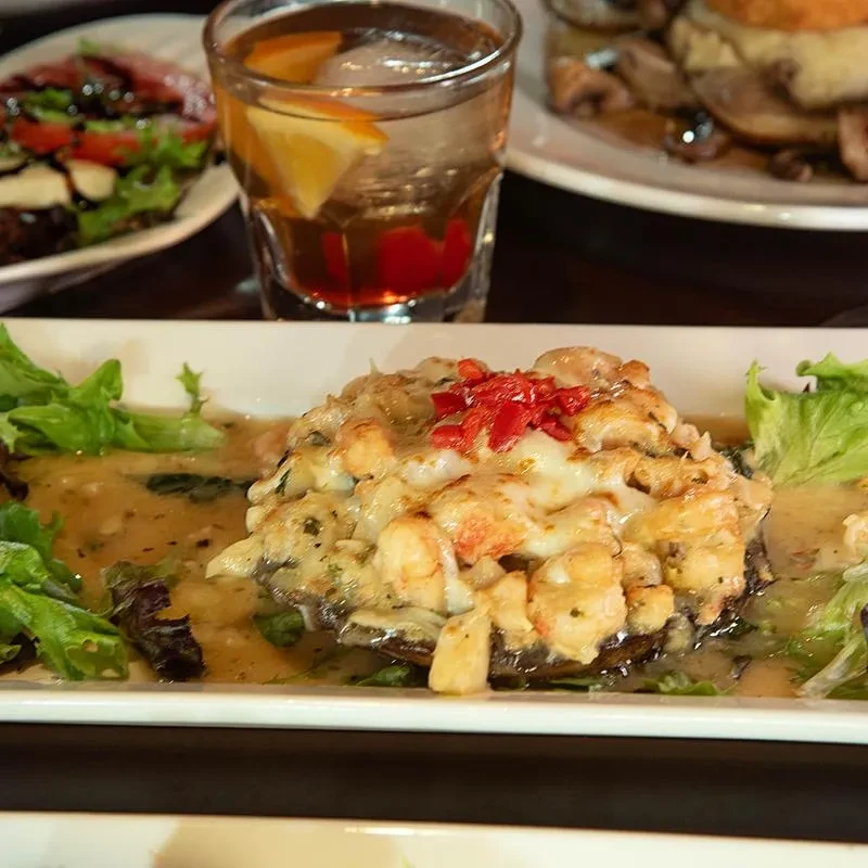 Close-up of a seafood-stuffed mushroom, a cocktail, and other restaurant dishes.