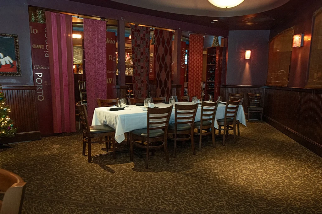 Empty upscale restaurant with long set table, wine curtains, Christmas tree.