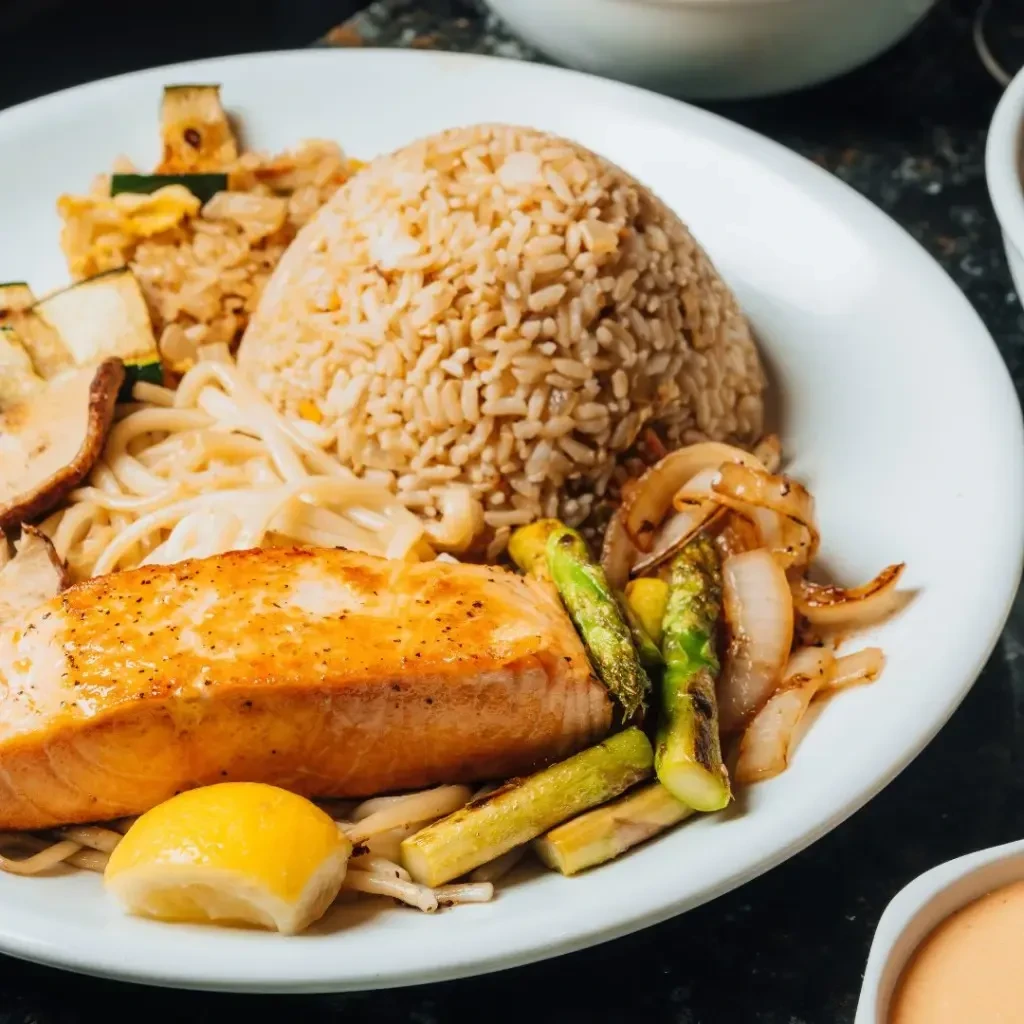 Grilled salmon, brown rice, noodles, and grilled vegetables on a plate.