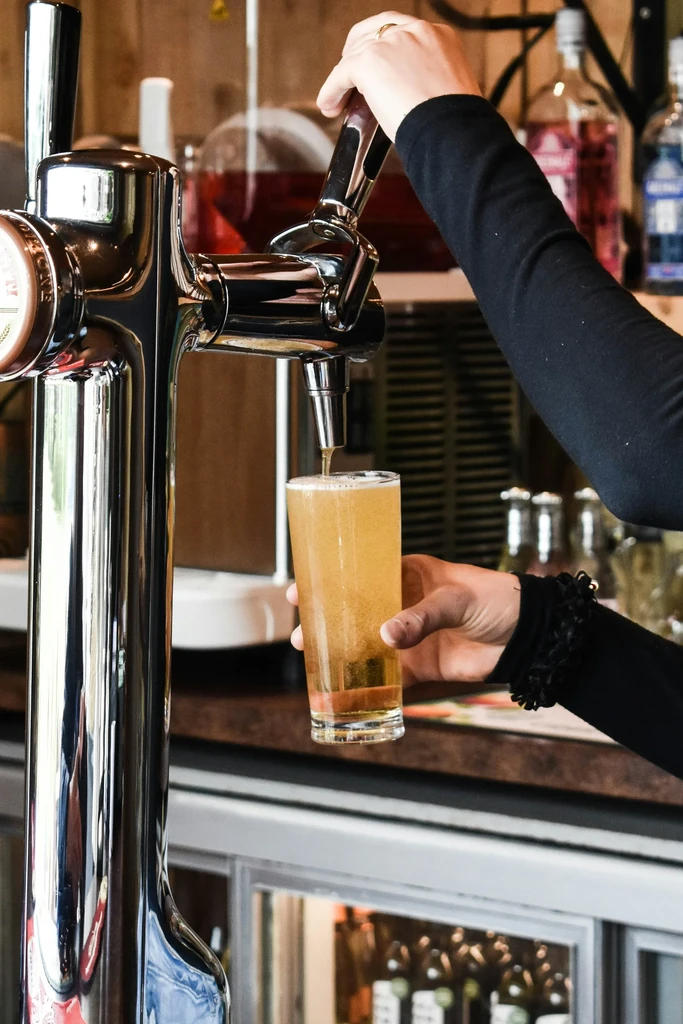 Two hands pouring amber beer from a chrome tap into glass.