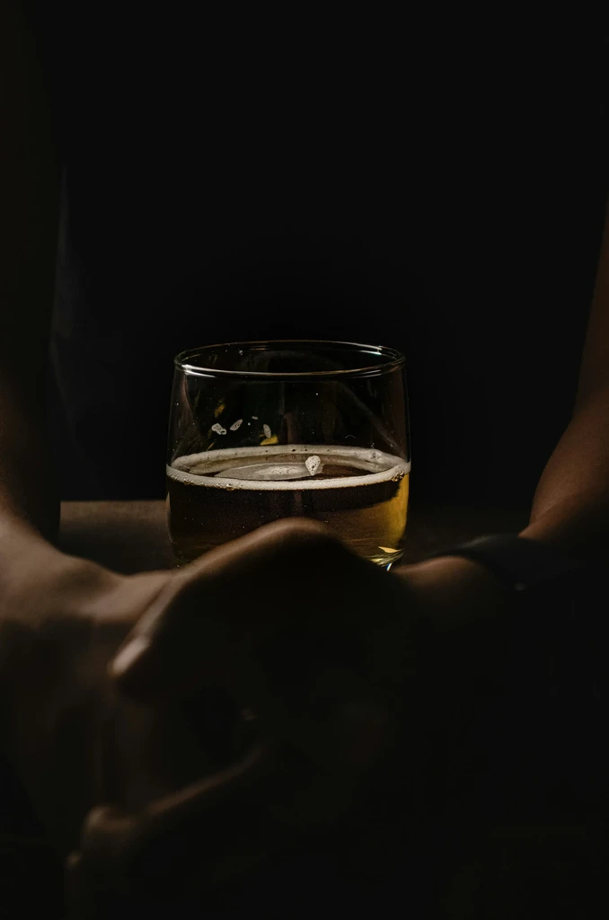 Golden beer with foam in glass, hands on dark wood.