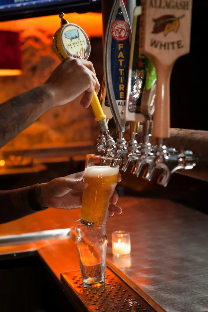 Bartender's hands pour golden beer from a tap into a pint.