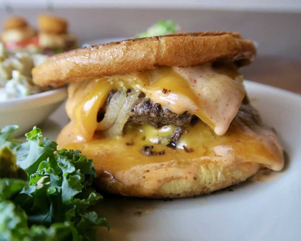Double-patty burger with melted cheese, sauce, onions, and greens.