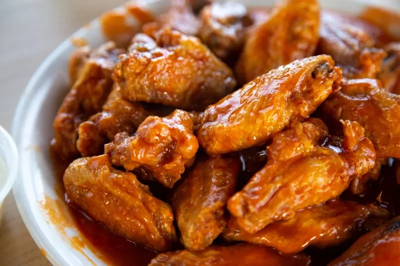 Piled buffalo chicken wings with glossy orange-red sauce on a plate.