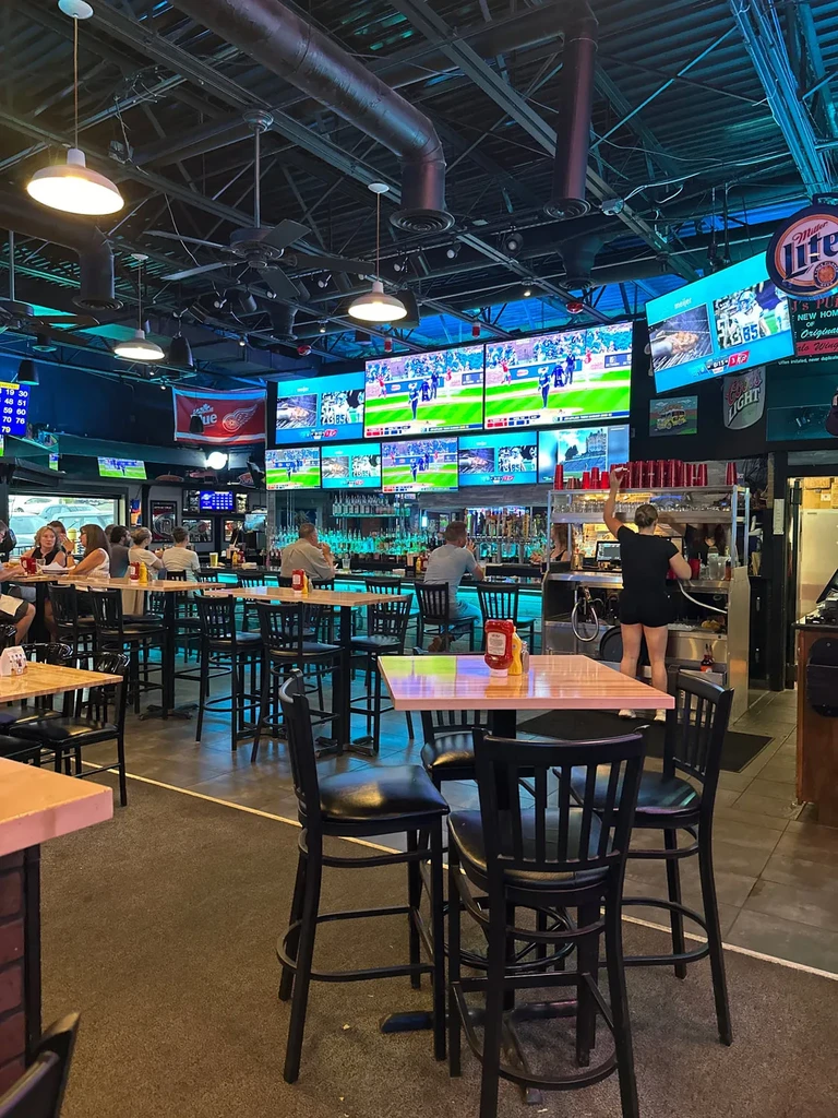 Busy sports bar interior with many TVs, high-top tables, and a bar.