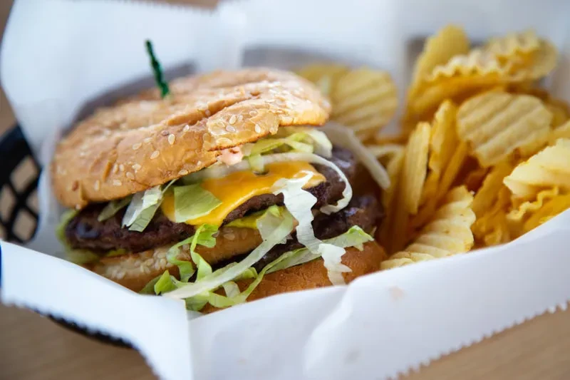 Double cheeseburger with crinkle-cut potato chips in a basket.