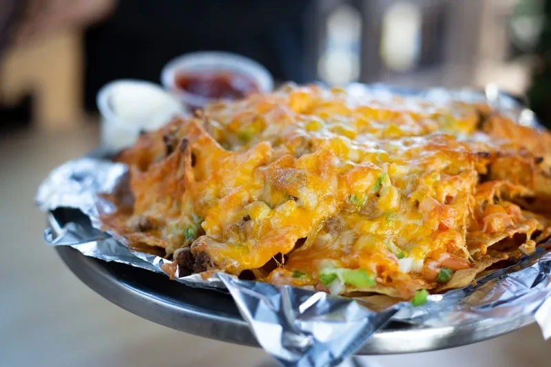 Close-up of fully loaded nachos with melted cheese, meat, and colorful toppings.