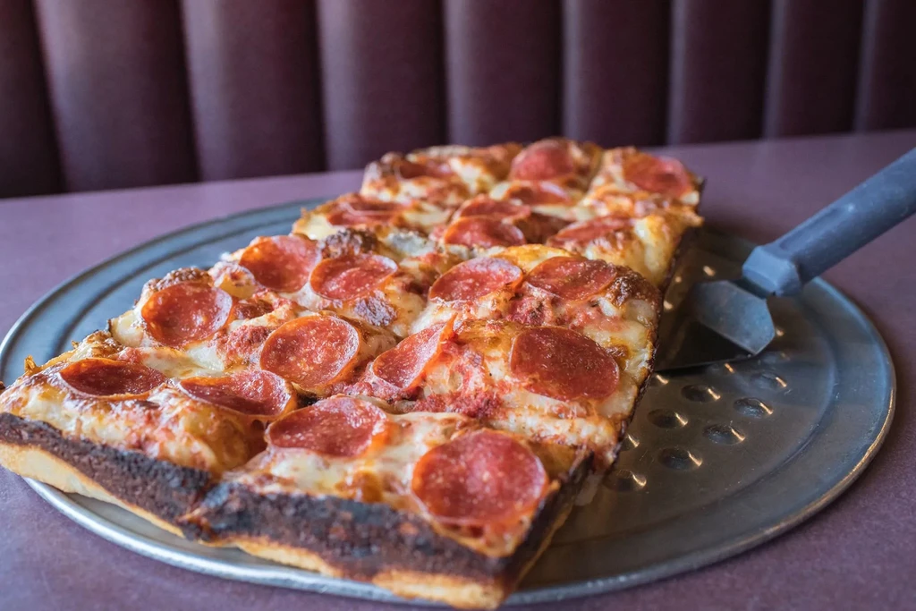 Square pepperoni pizza slices on a metal pan with a server.