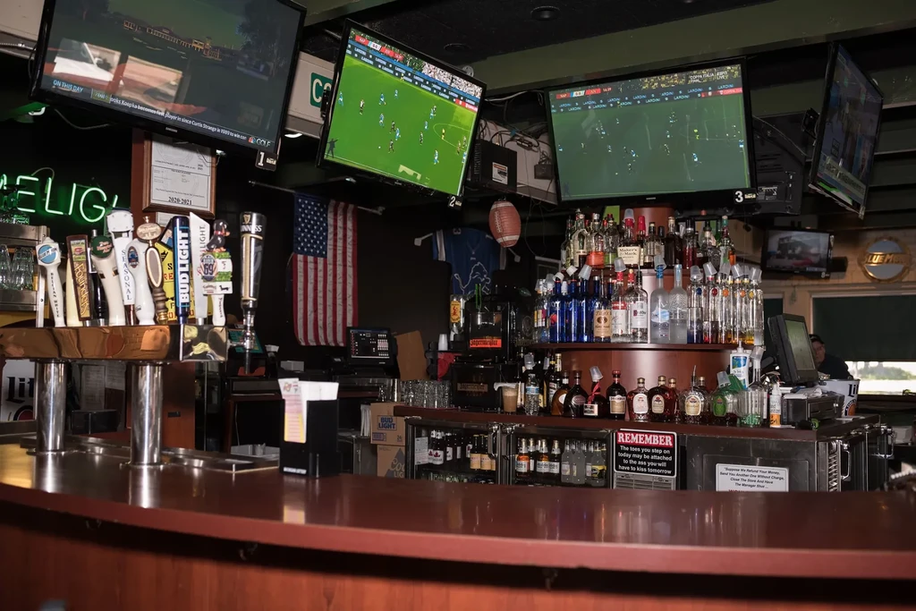 Bustling sports bar interior with beer taps, liquor bottles, and TVs.