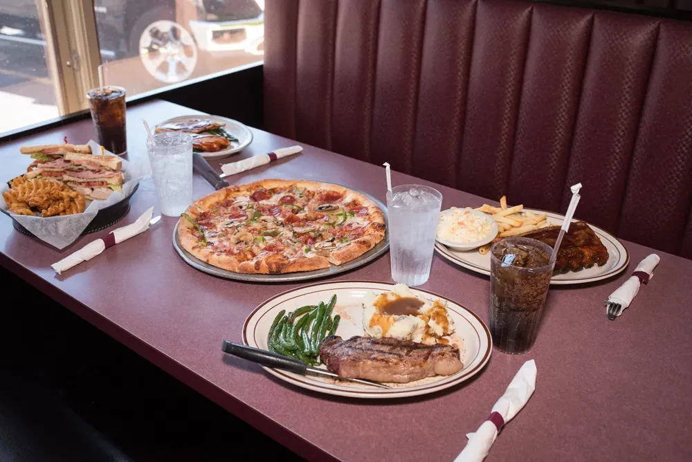 Diner table with pizza, club sandwich, ribs, steak, and sides.