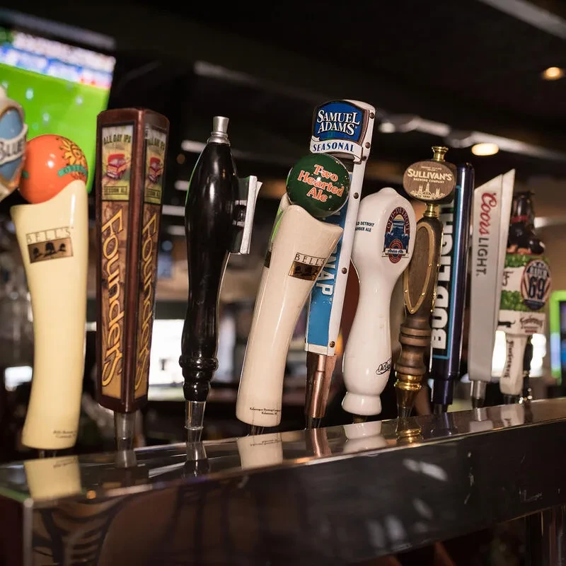 A close-up of many branded beer tap handles on a bar.
