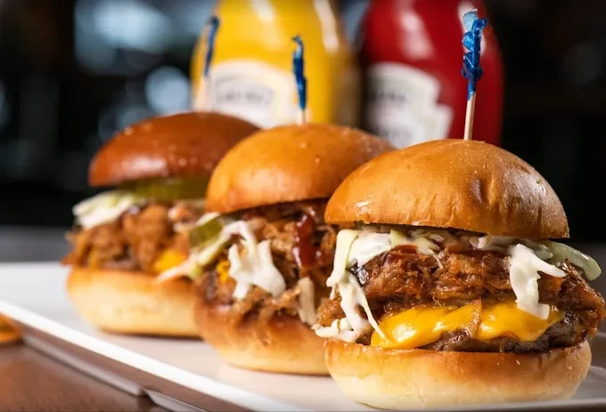 Three pulled pork sliders with cheese and coleslaw on a white plate.