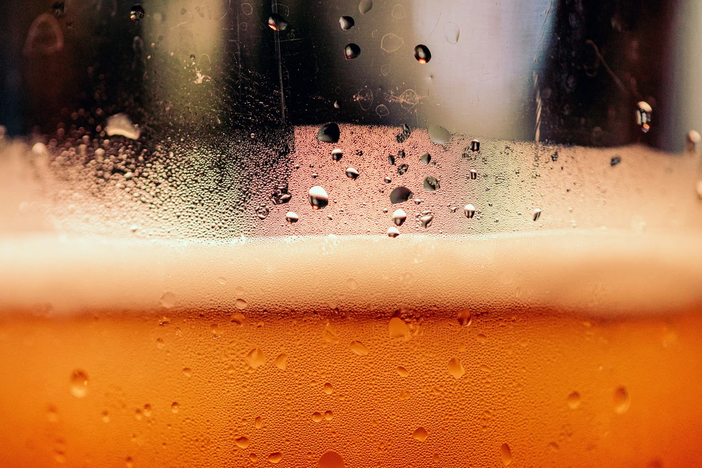Macro close-up of amber beer in a glass with foam and condensation.