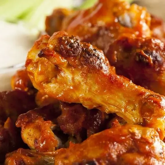 Close-up of crispy Buffalo chicken wings with red sauce, dip, and celery.