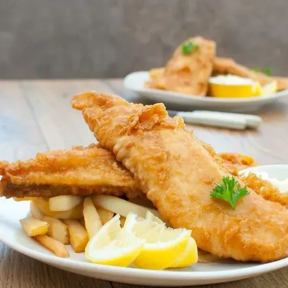 Golden battered fish fillets, thick-cut fries, lemon, and parsley.