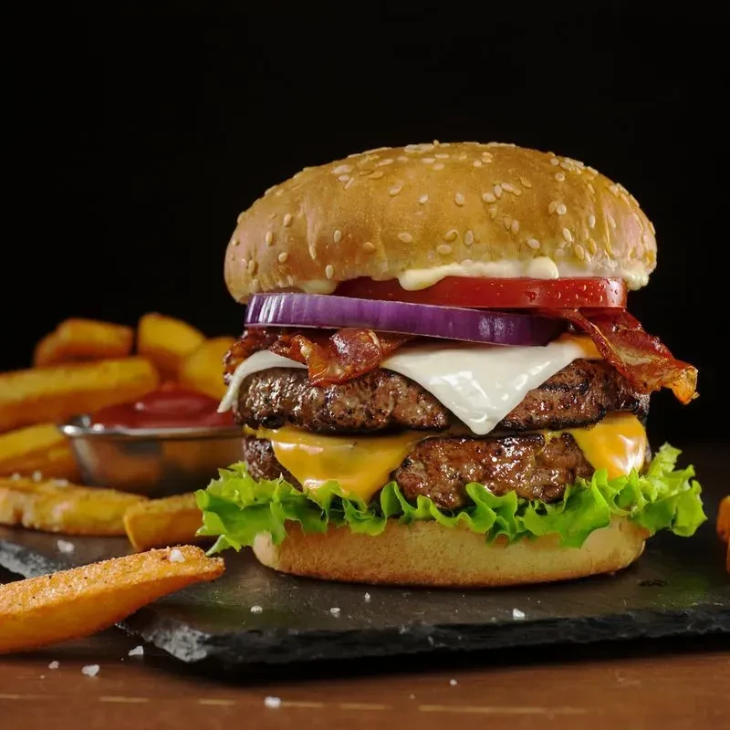 Double cheeseburger with melted cheese, fries, and ketchup on a dark surface.