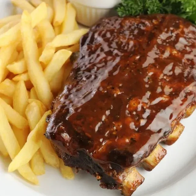Close-up of barbecued ribs and french fries on a white plate.