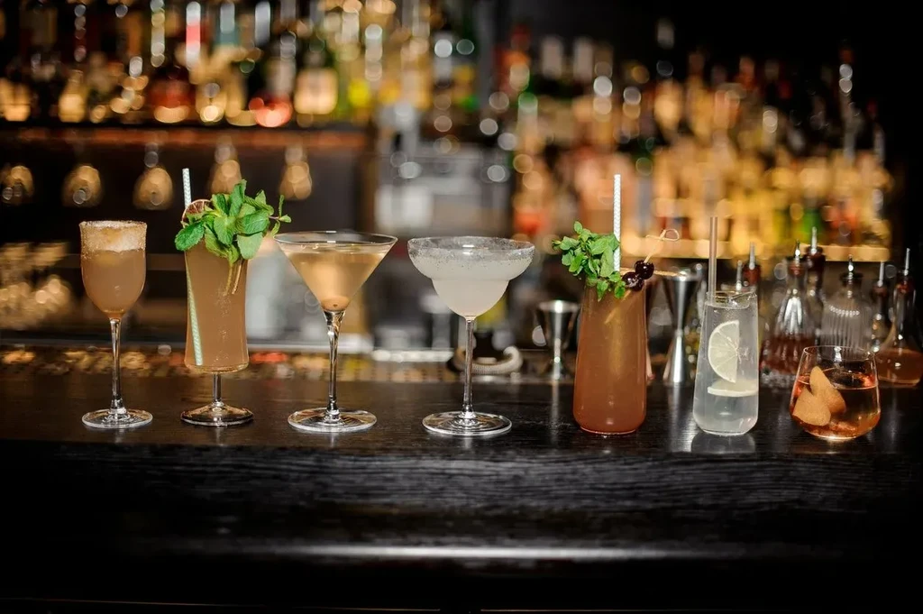 Seven distinct cocktails with garnishes on a dark bar counter.