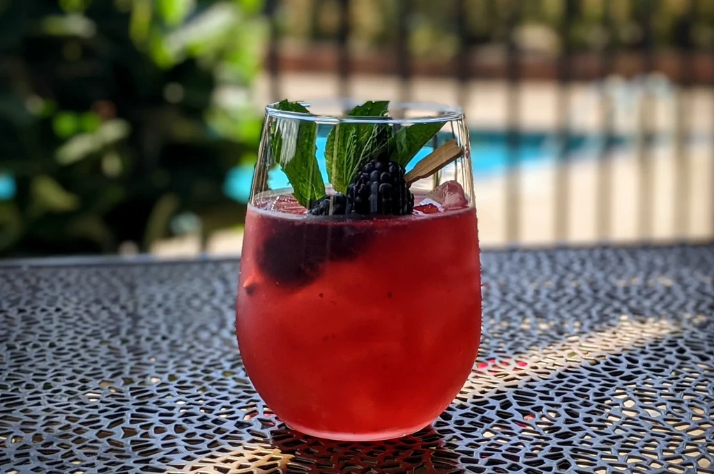 Close-up of a red berry drink with mint and ice, poolside.