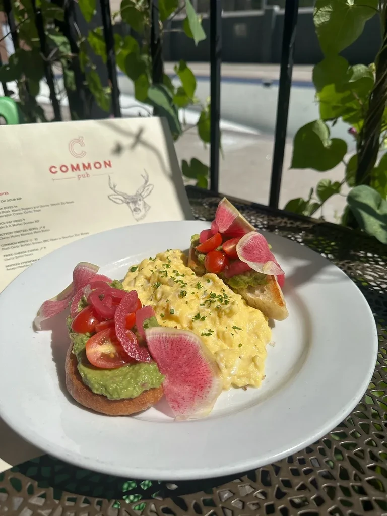 Outdoor plate with scrambled eggs, avocado toast, and pink pickled onions.