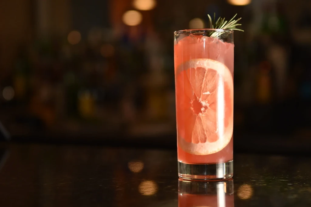 Close-up of a pink cocktail with grapefruit and rosemary garnish.
