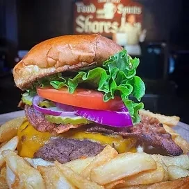 Close-up of a large cheeseburger with bacon, vegetables, and fries.