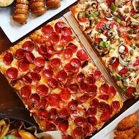 Top-down view of two rectangular pizzas, pretzel twists, and fried chicken.