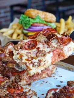 Spatula lifts cheesy deep-dish pizza slice, with burger and fries.