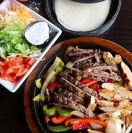 Sizzling steak and chicken fajitas with peppers, onions, toppings, and tortillas.