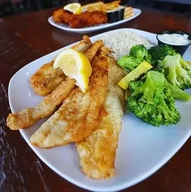 Pan-fried fish fillets, rice, broccoli, lemon, and tartar sauce on a plate.