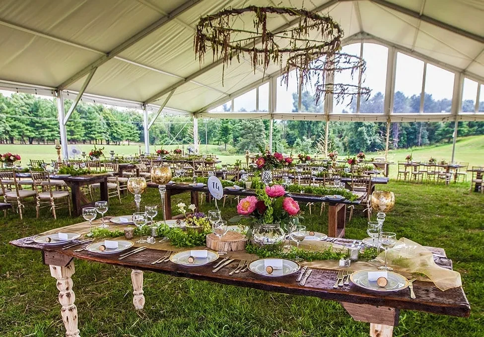 Decorated tent with rustic dining tables, floral arrangements, and green hills.