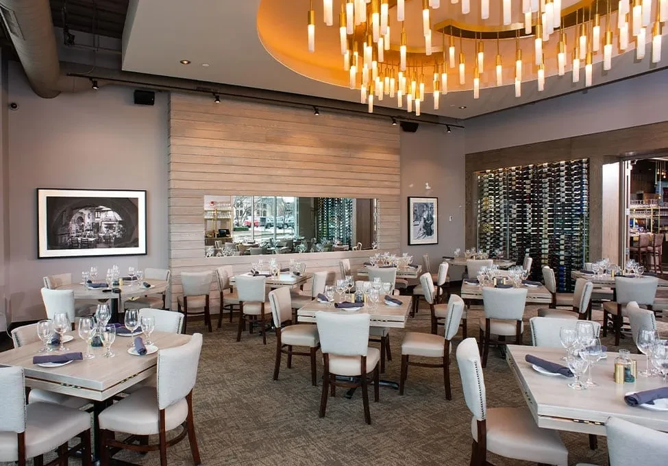Sophisticated restaurant dining area with modern chandelier, set tables, and wine wall.