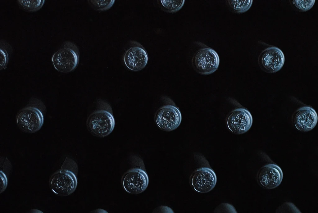 Close-up of dark wine bottle tops with embossed grape designs in a grid.